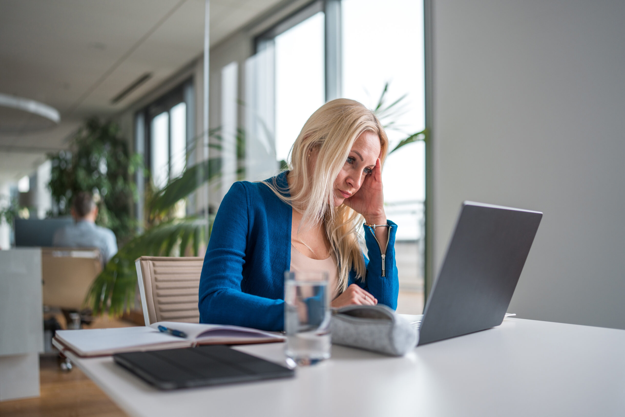 Eine Person sitzt an einem Schreibtisch, hält ihren Kopf und schaut auf ihren Laptop