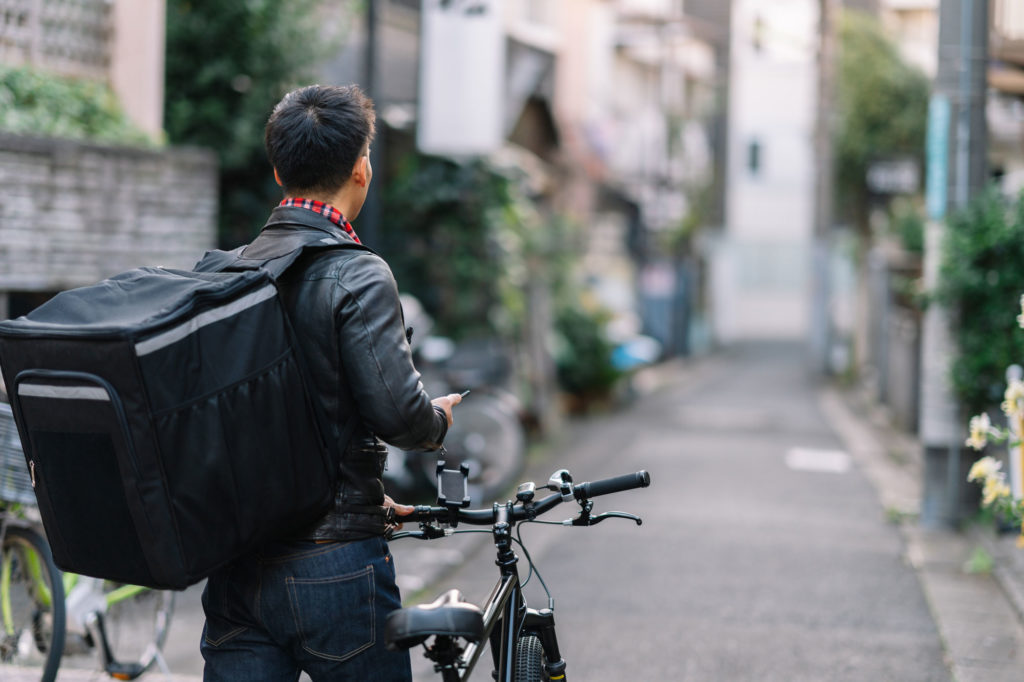 A delivery worker uses a phone while standing with a bike