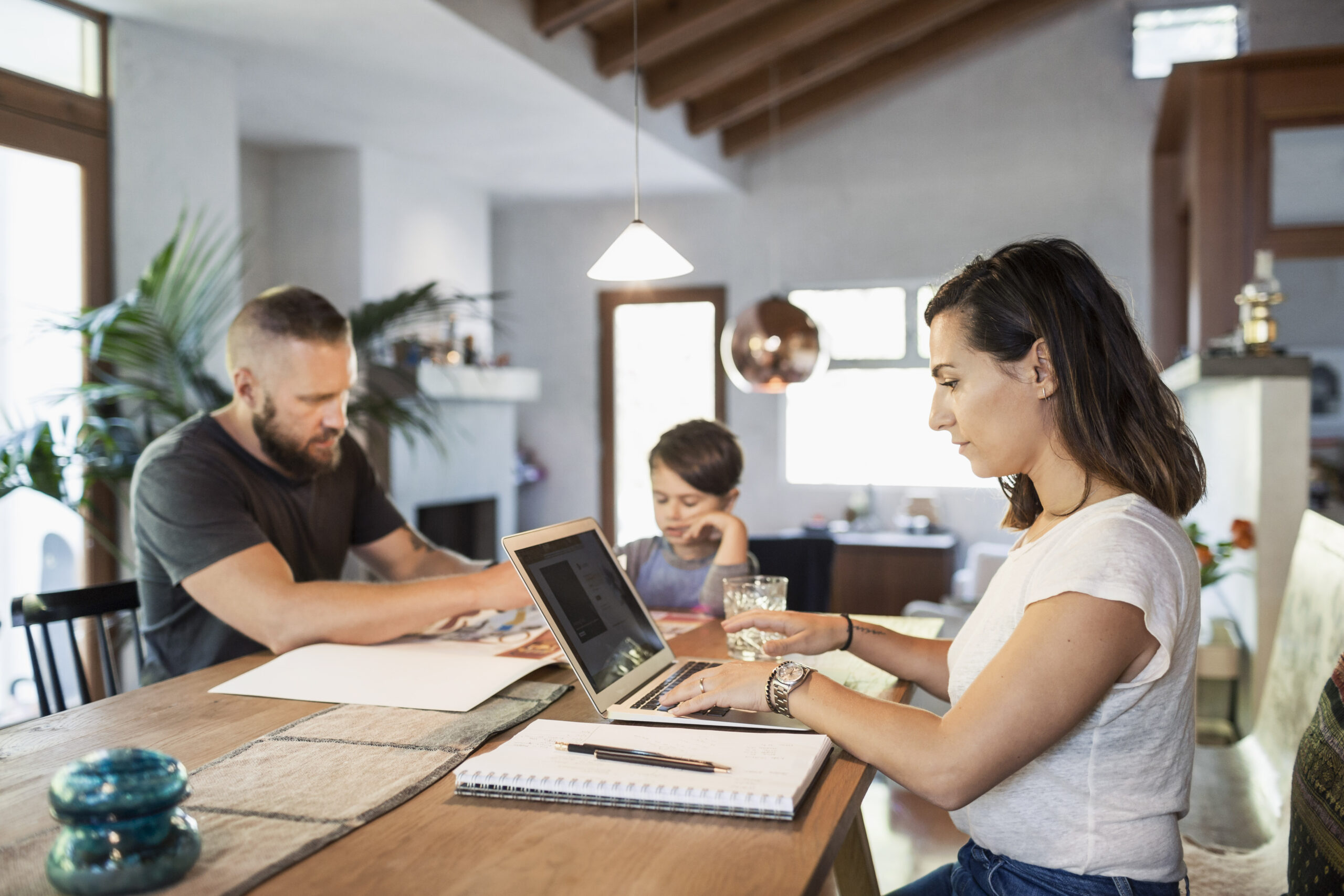Parents working from home at the dining table with their child alongside them