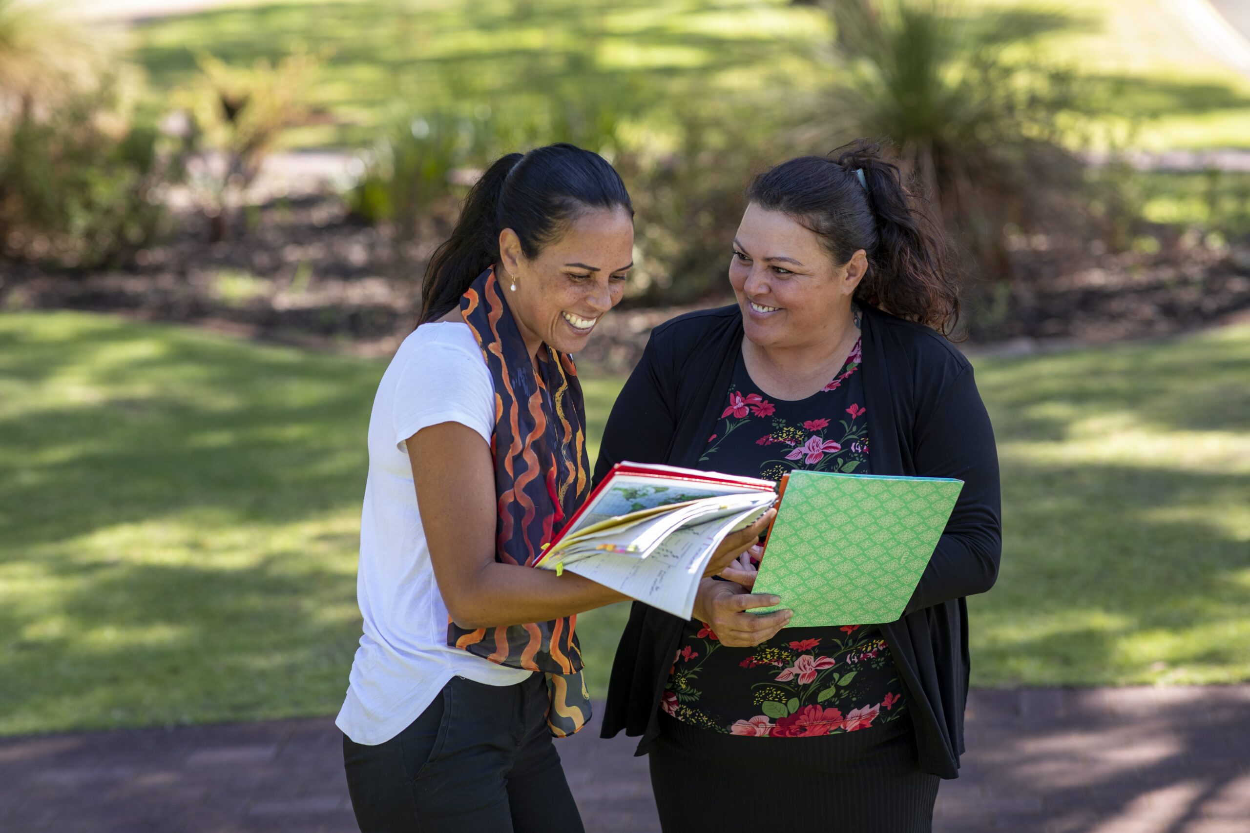 Two people smiling outdoors both holding folders
