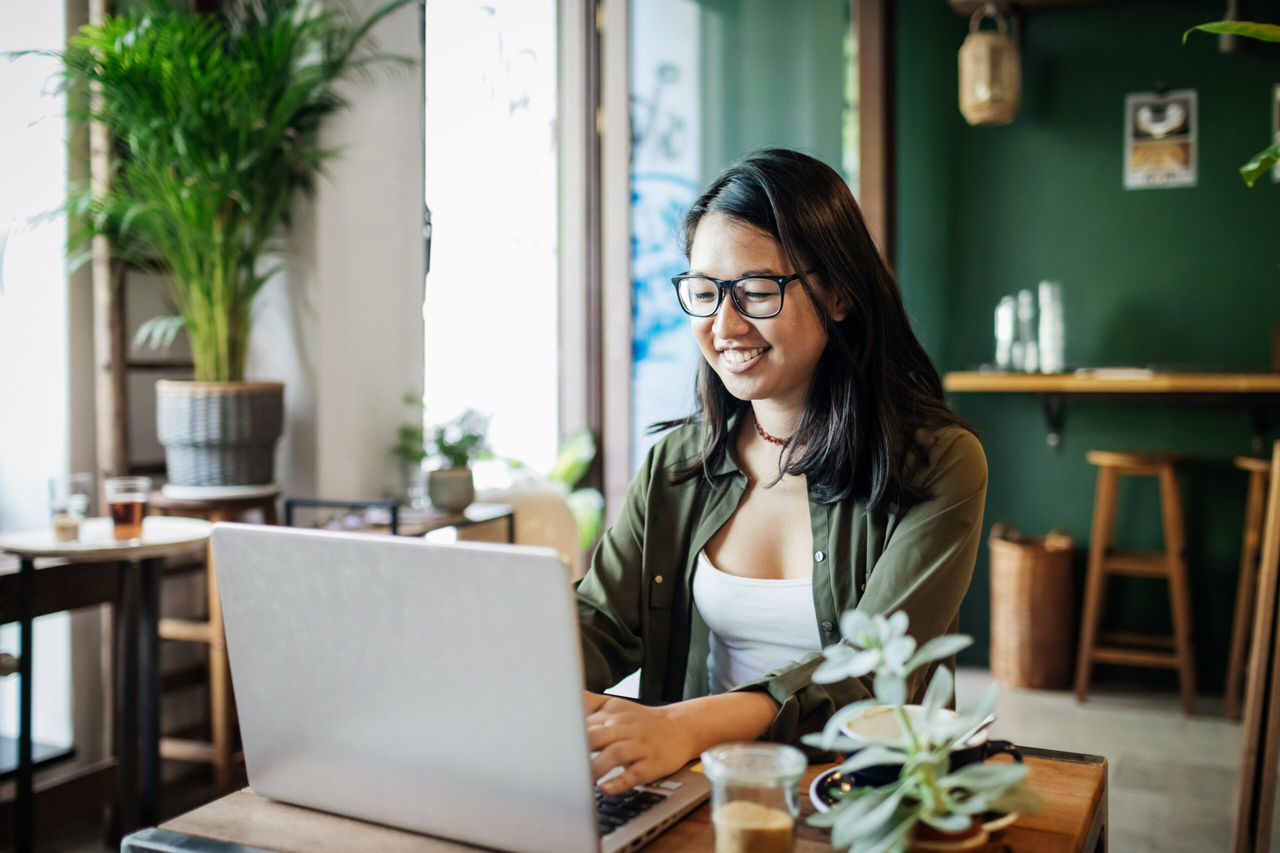 A young person smiling whlie working on her laptop in a cafe