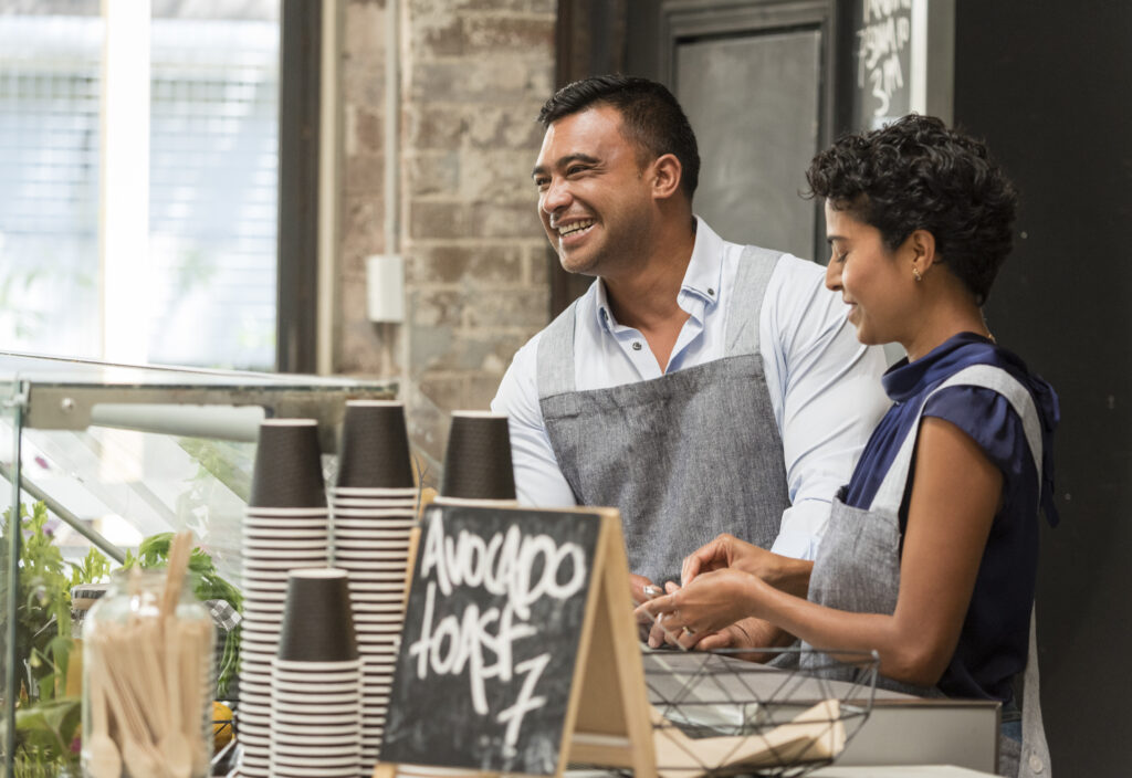 Picture shows two young people behind the counter serving coffee in their open airy cafe.