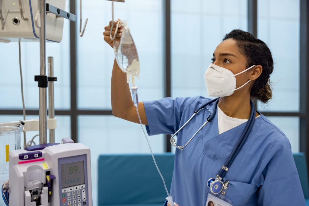 Nurse wearing a mask hanging an IV bag drip in the hospital