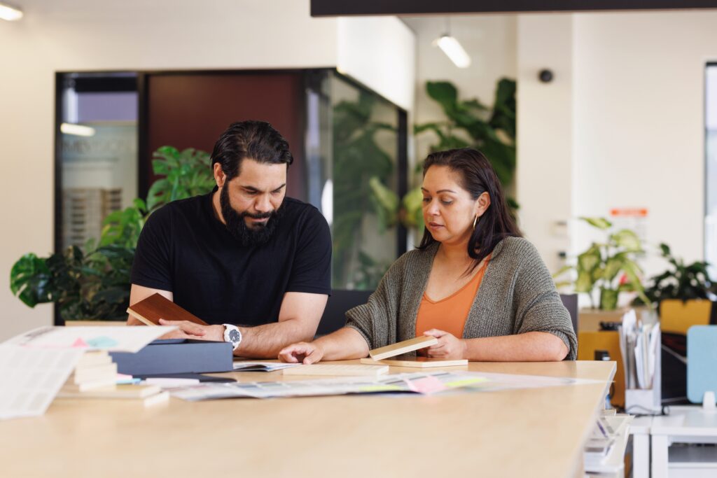 Two people collaborating sitting at desk looking at books in open workspace office