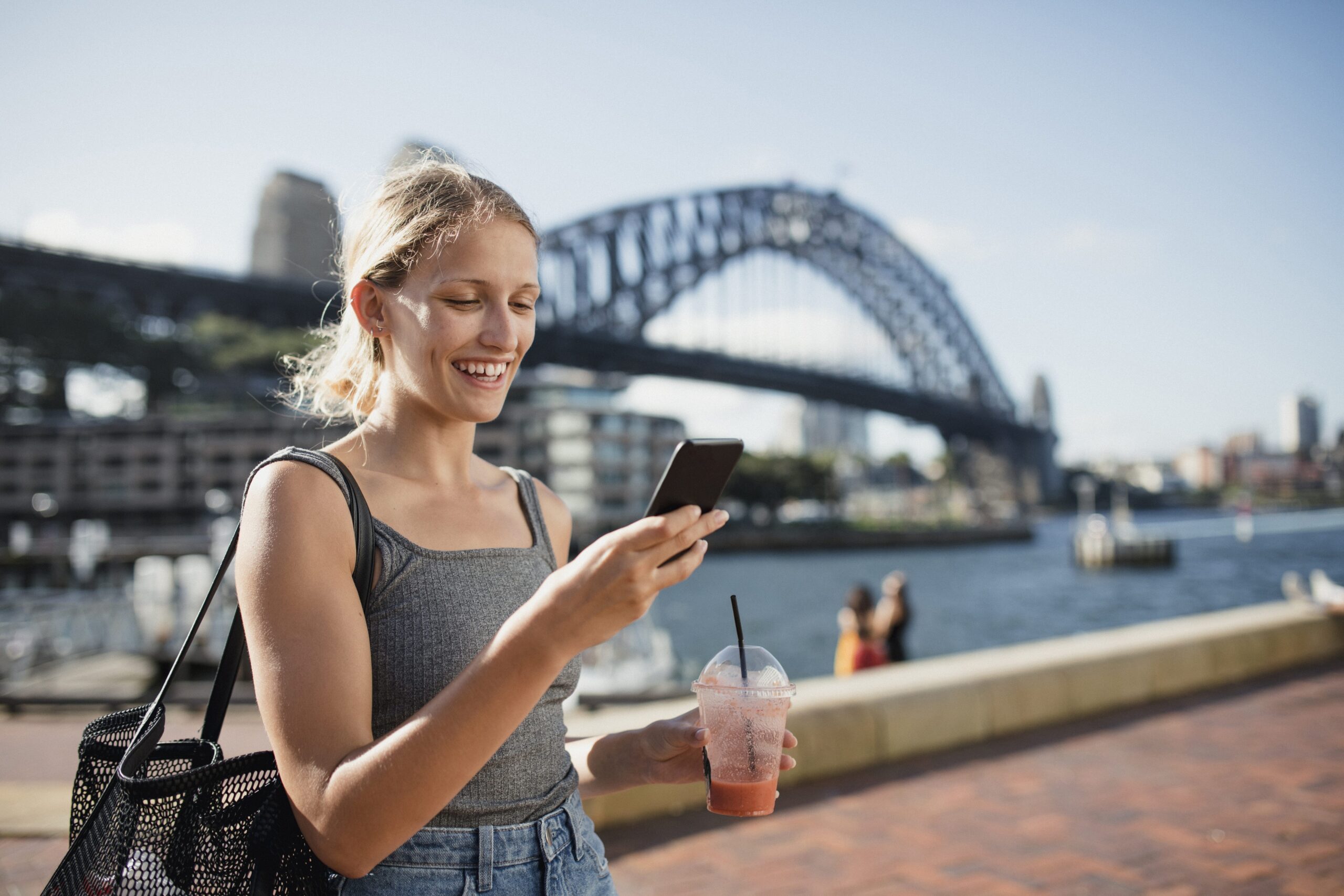 Young person smiling while texting in front of Sydney Harbour Bridge