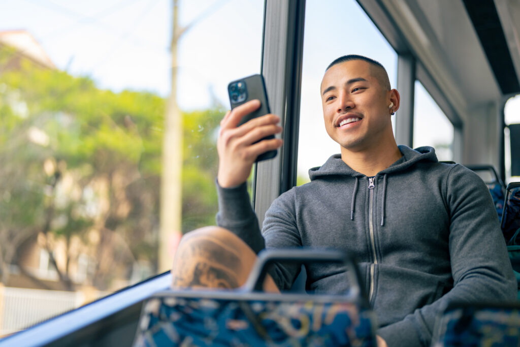 Young person smiling and looking at their phone while riding on a bus