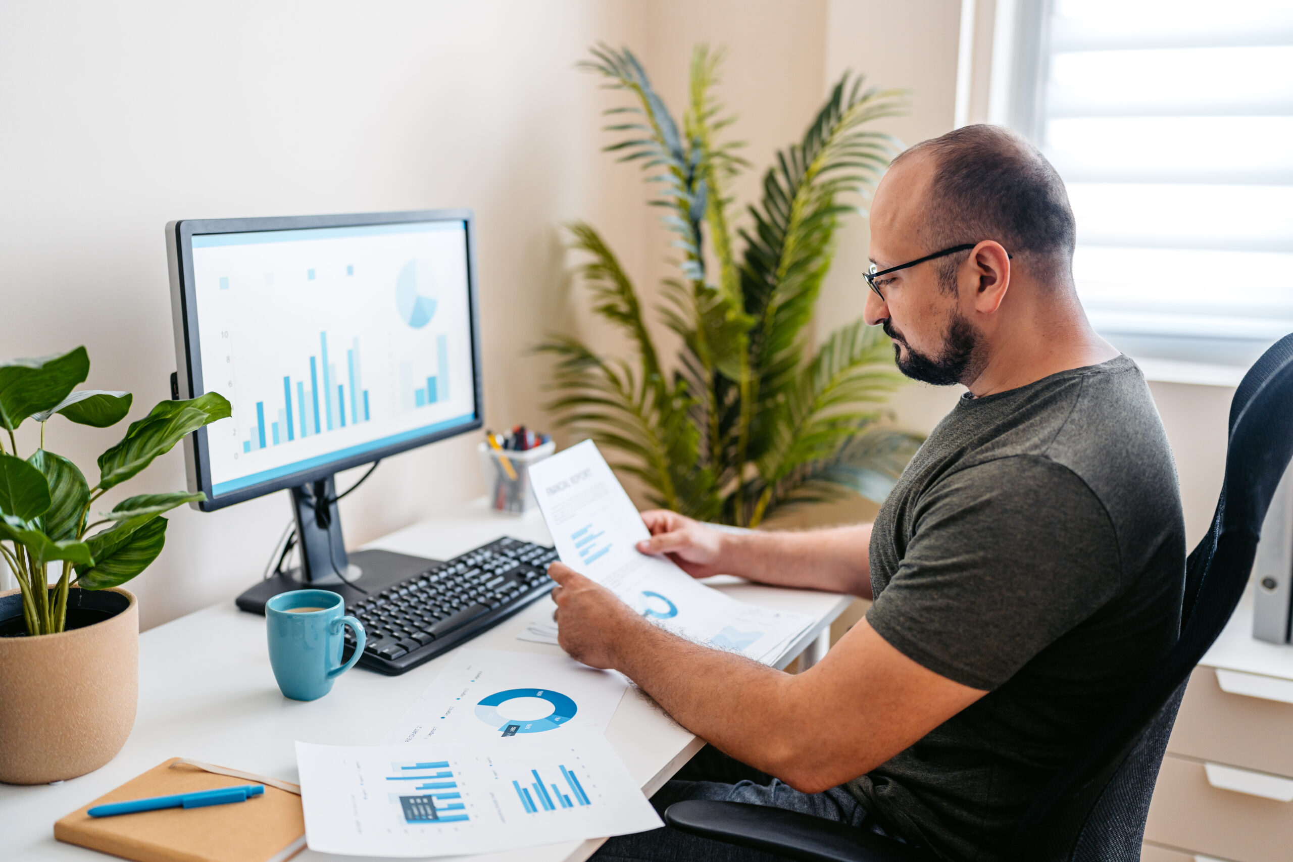 Person sitting at home going over paperwork at their desk, working remotely, with their computer on the desk