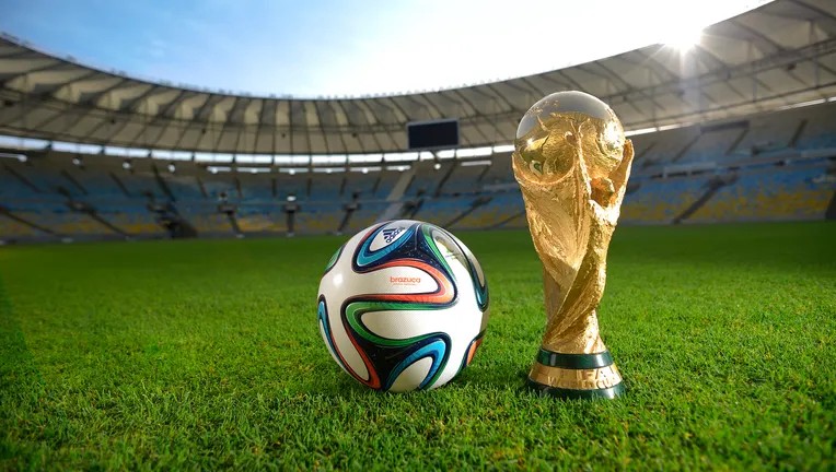 The World Cup and a soccer ball sitting on the turf in a stadium