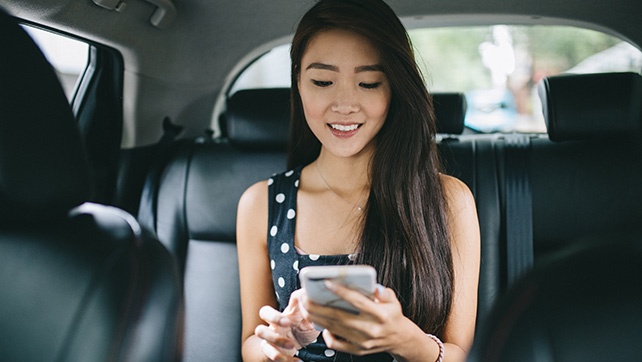 車の後部座席でモバイル端末を見て微笑んでいる人物。