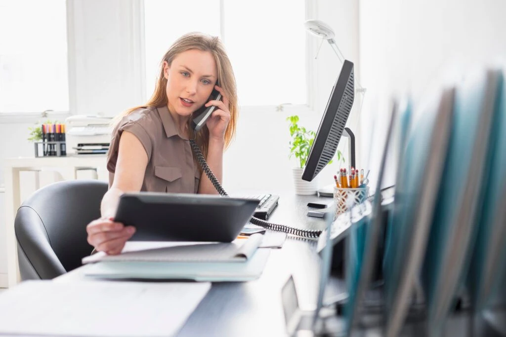 Mitarbeiterin telefoniert im Büro und arbeitet gleichzeitig mit einem Tablet und Computer