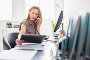 Mitarbeiterin telefoniert im Büro und arbeitet gleichzeitig mit einem Tablet und Computer