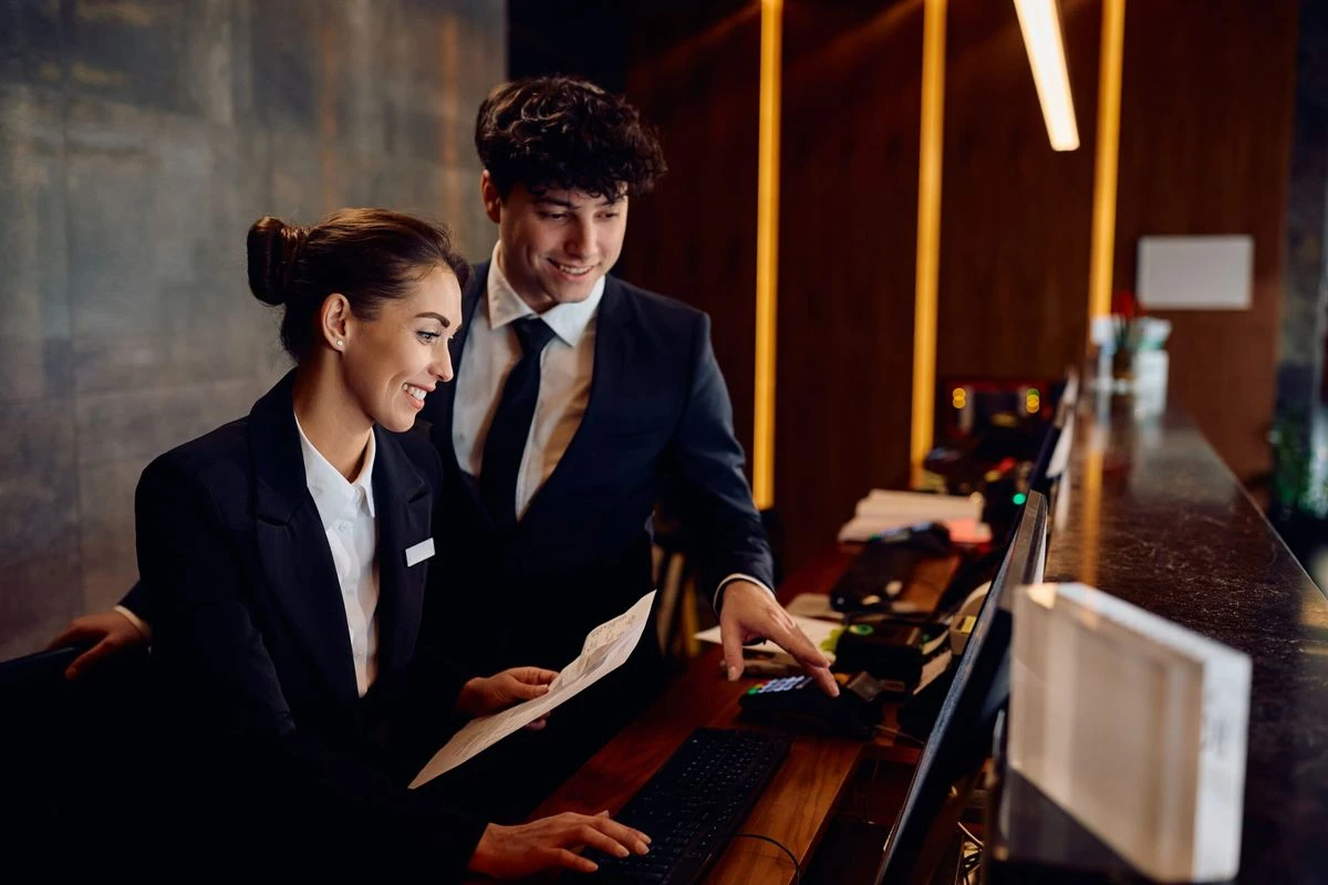 Zwei Hotelmitarbeiter arbeiten gemeinsam an der Rezeption und prüfen Reservierungsunterlagen am Computer